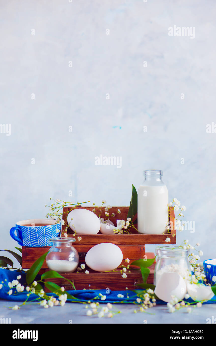 Concept de cuisine à domicile avec des ingrédients, des œufs, du lait, de la farine sur un fond clair. Les caisses en bois et fleurs de gypsophile. Banque D'Images