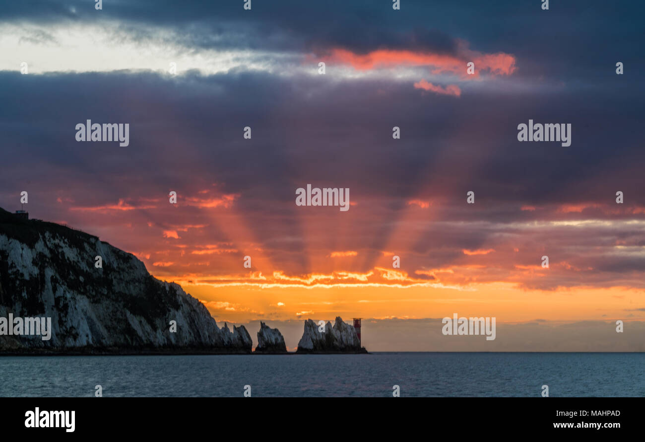 Coucher du soleil derrière les aiguilles Starburst rocks et le phare, de l'Alun Bay, île de Wight. Une étoile scintillante de rayons rouges irradiant derrière les rochers. Banque D'Images