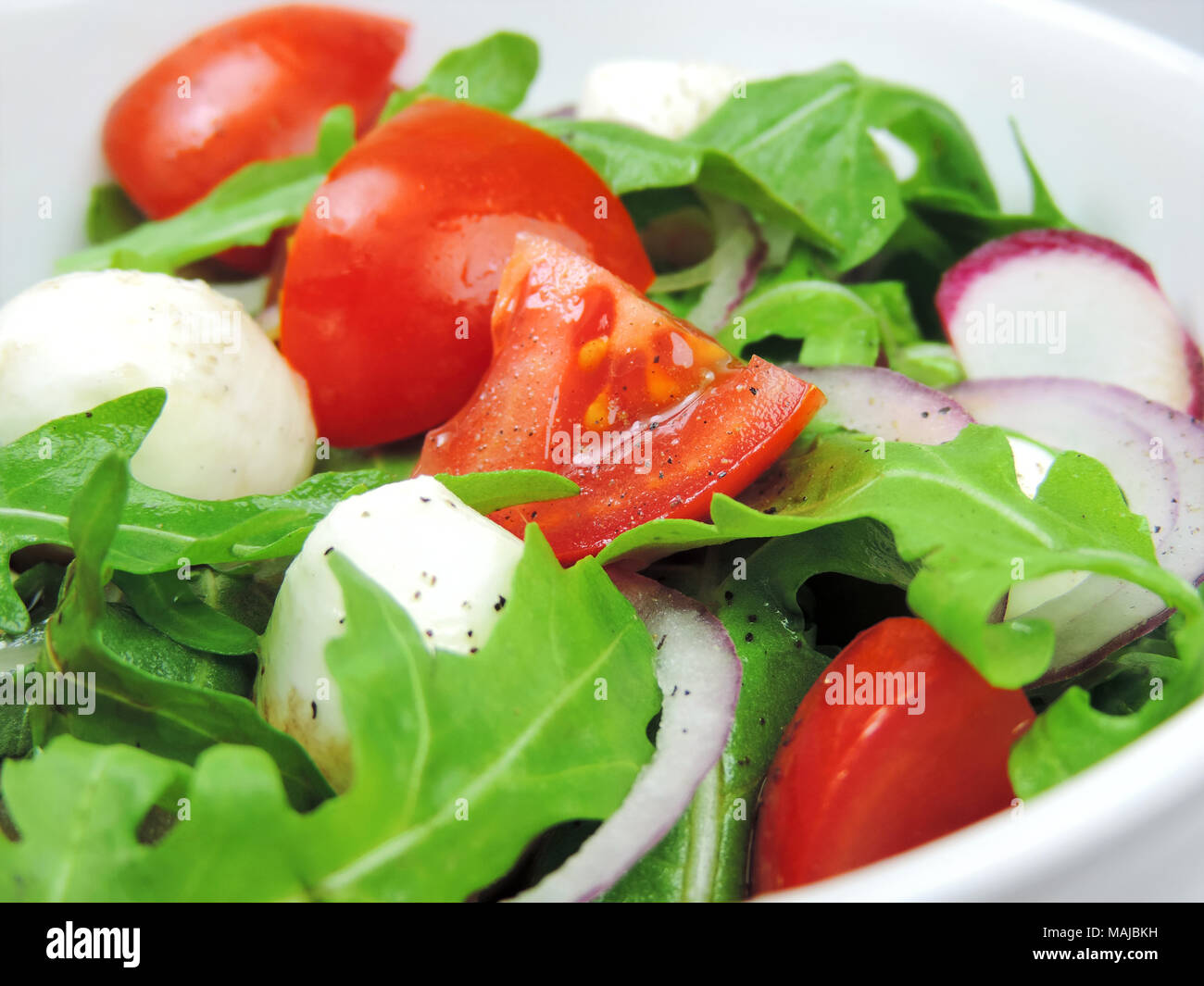 Salade gourmande ou frais salade caprese avec tomates, oignons rouges, roquette et mozzarella fromage sur une assiette blanche. Gros plan de salade fraîche. Banque D'Images