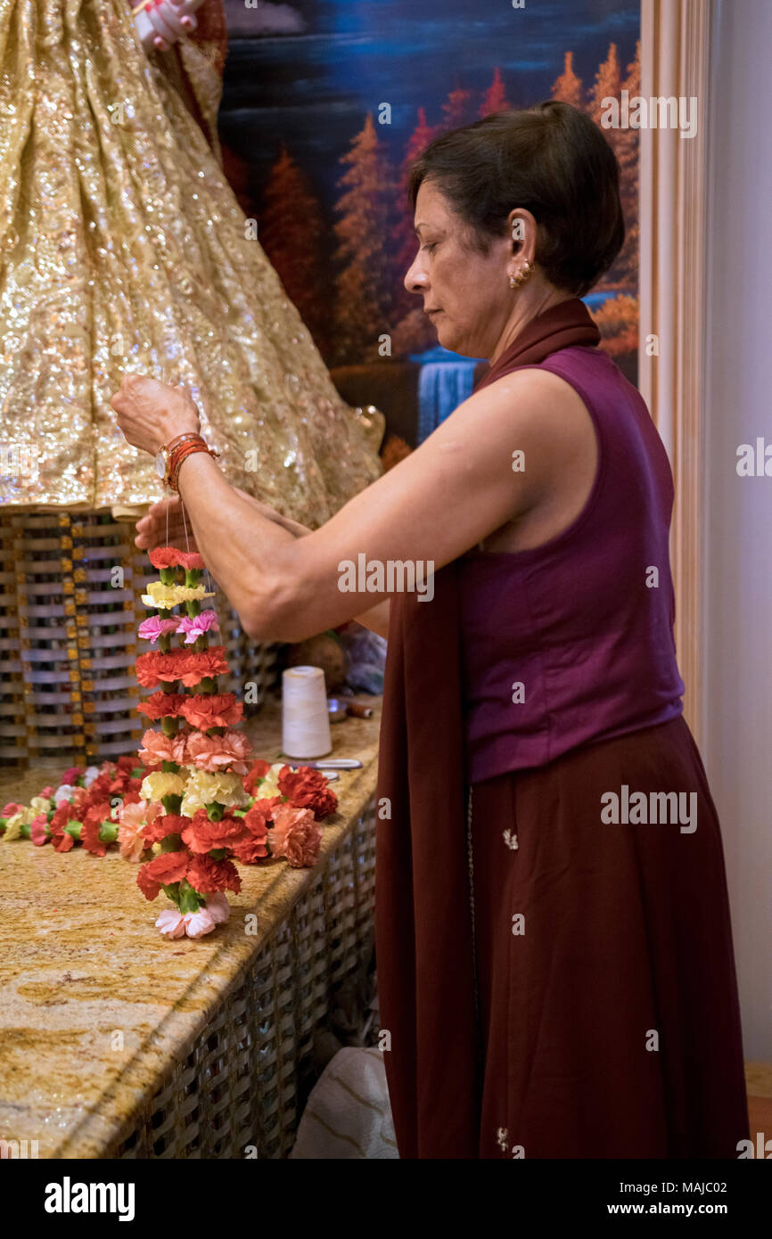 Un adorateur à un temple hindou coud fleurs ensemble pour être utilisé dans un dimanche matin de prière. Je Richmond Hill Queens, New York. Banque D'Images