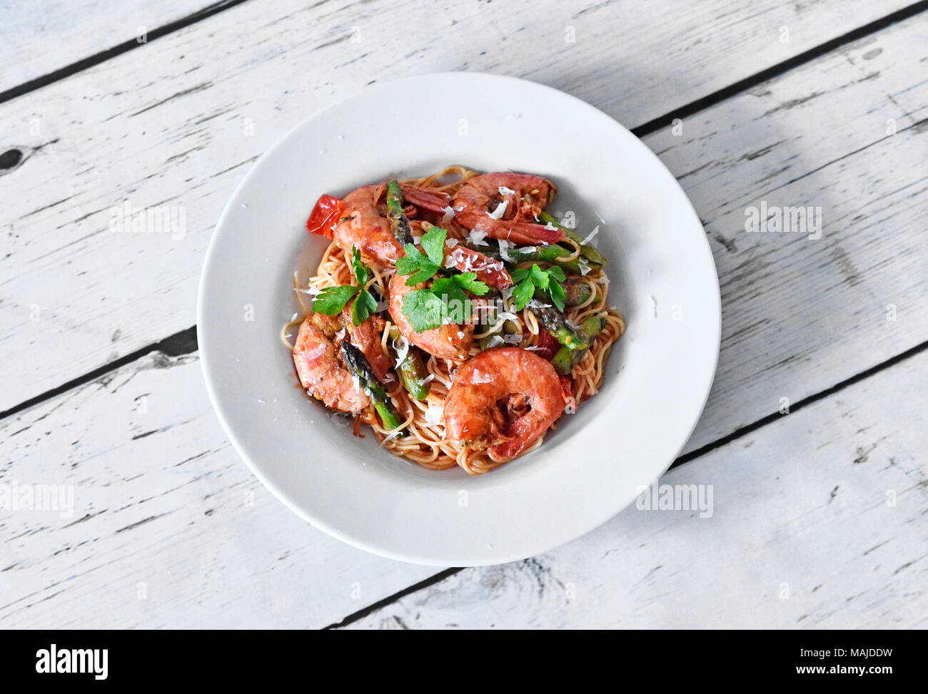 Plaque de tapas frais aux crevettes et asperges vertes, tranche de citron et le persil. Plat gastronomique sur une table en bois blanc. Banque D'Images