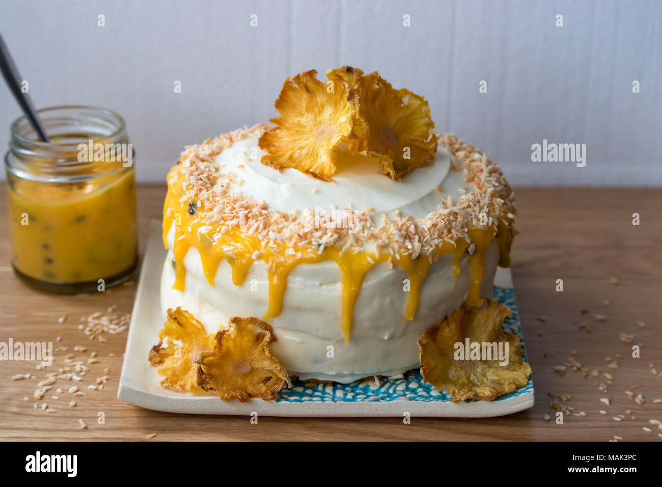 Un gluten free, ananas et noix de coco aux fruits de la passion gâteau caillé. Décorées avec des fleurs ananas séché et affichés sur une plaque à la main. Banque D'Images