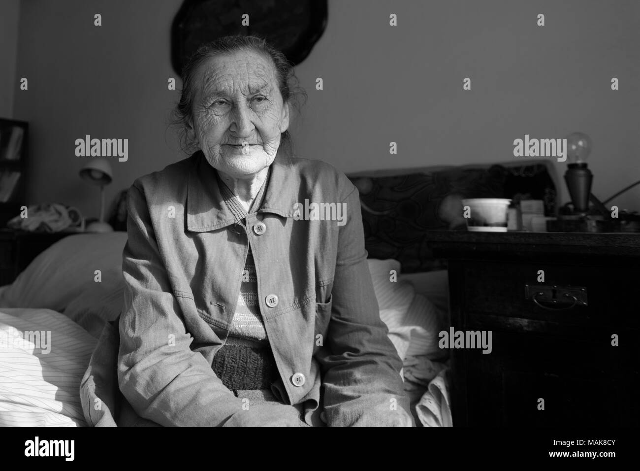 80 plus beaux ans senior woman portrait. Image en noir et blanc de personnes âgées inquiète femme assise sur un lit dans une maison de soins infirmiers. Banque D'Images