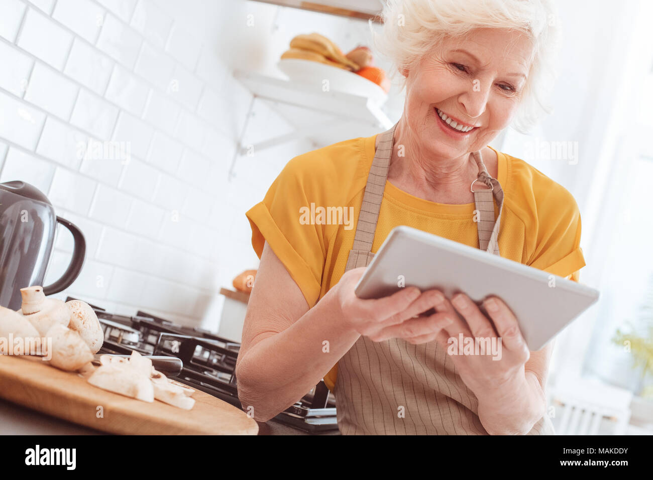 Pensionné woman holding tablet, regardant la vidéo ou lisez le livre dans l'internet. Piscine, studio tournage, cuisine intérieur Banque D'Images