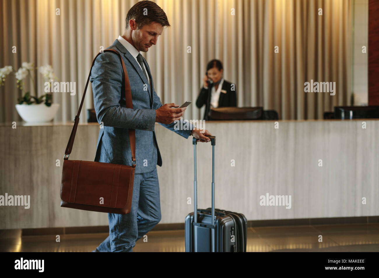 Young businessman walking dans le hall de l'hôtel et à l'aide de téléphone mobile. Voyageur d'arriver à son hôtel. Banque D'Images