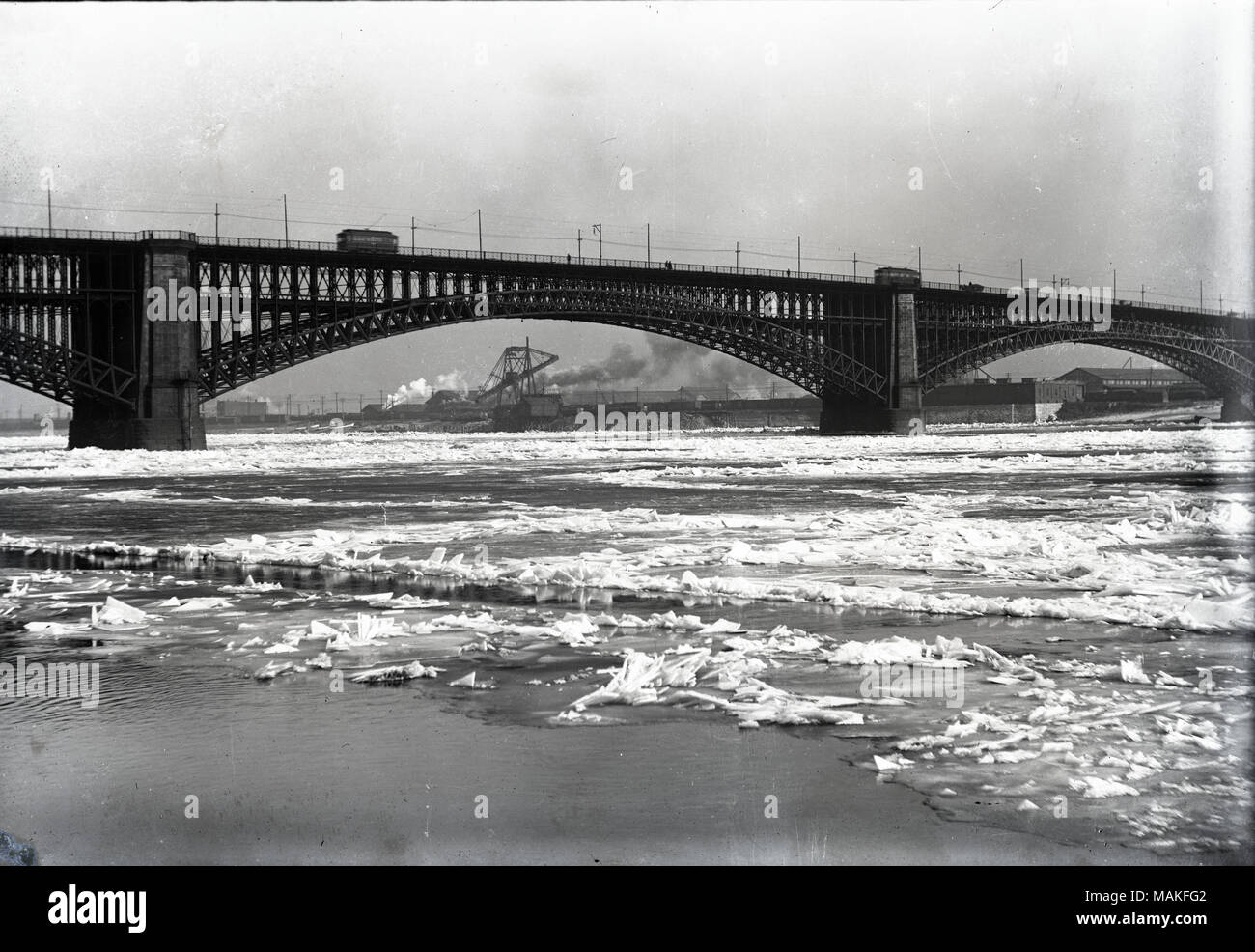 Scène d'hiver du pont Eads tourné à partir de l'Ohio riverfront. Il y a l'écoulement des glaces sur le fleuve Mississippi. Vous voyez des chariots sur le pont supérieur du pont et de l'épaisse fumée des usines sur le côté de la rivière de l'Illinois. Titre : Pont d'Eads, Janvier, 1917. . Janvier 1917. Oscar Kuehn Banque D'Images