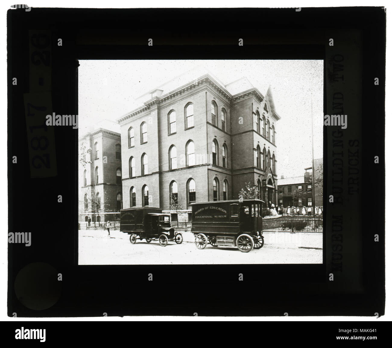 À l'horizontal, photo en noir et blanc de trois étages en brique, montrer aux enfants la queue pour entrer dans la porte avant. Deux camions sont garés sur le trottoir à côté du bâtiment. Titre : Musée des diapositives sur l'éducation : l'éducation Musée et deux camions. . Vers 1900. Banque D'Images