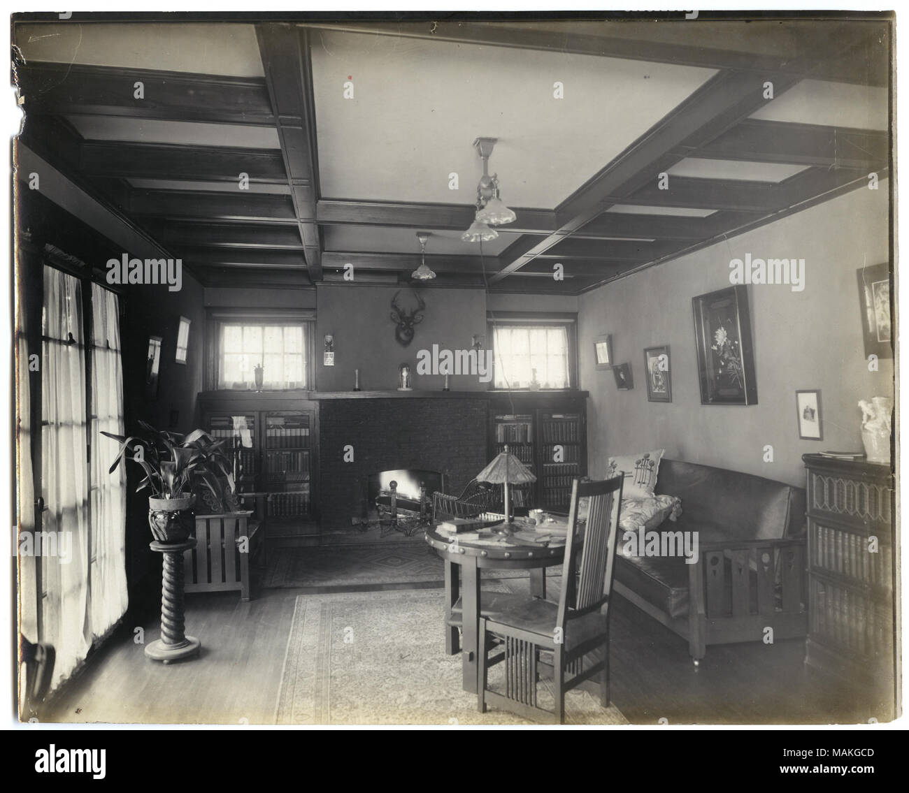 Photographie sépia, Horizontal montrant une chambre avec portes en verre à gauche, construit en bibliothèques de chaque côté d'une cheminée allumée, et d'un canapé et d'une petite table et chaise situé sur la droite. Titre : Petit salon intérieur avec décoration de style mission et cheminée. . Vers 1900. Robert Walter Banque D'Images