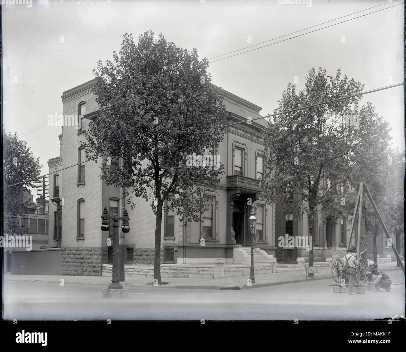L'horizontale, 1970 Photographie noir et blanc montrant un quartier résidentiel de deux et trois étages de maisons en brique d'un bout à l'autre coin de rue. Au premier plan sur le côté droit, plusieurs hommes sont l'érection d'un lampadaire qui est suspendu sous une structure en bois. Un signe sur la structure lit ' l'approche la plus proche de la lumière naturelle. La lampe à arc de gaz.' Title : Installation du gaz lampes à arc à l'angle de Washington et Theresa Avenue. . Vers 1910. Banque D'Images