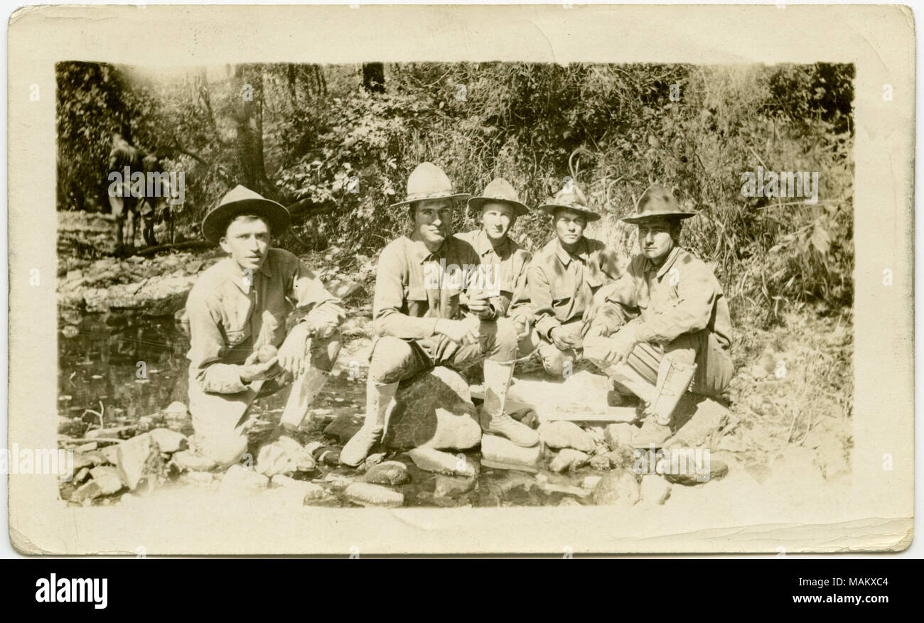 Photographie sépia, Horizontal montrant cinq soldats en uniforme assis sur le sol ou sur des rochers dans une région très boisée. Les soldats posent pour une photo de groupe. Titre : Cinq soldats posant pour une photo de groupe dans une région très boisée. . Entre vers 1916 et vers 1918. Banque D'Images