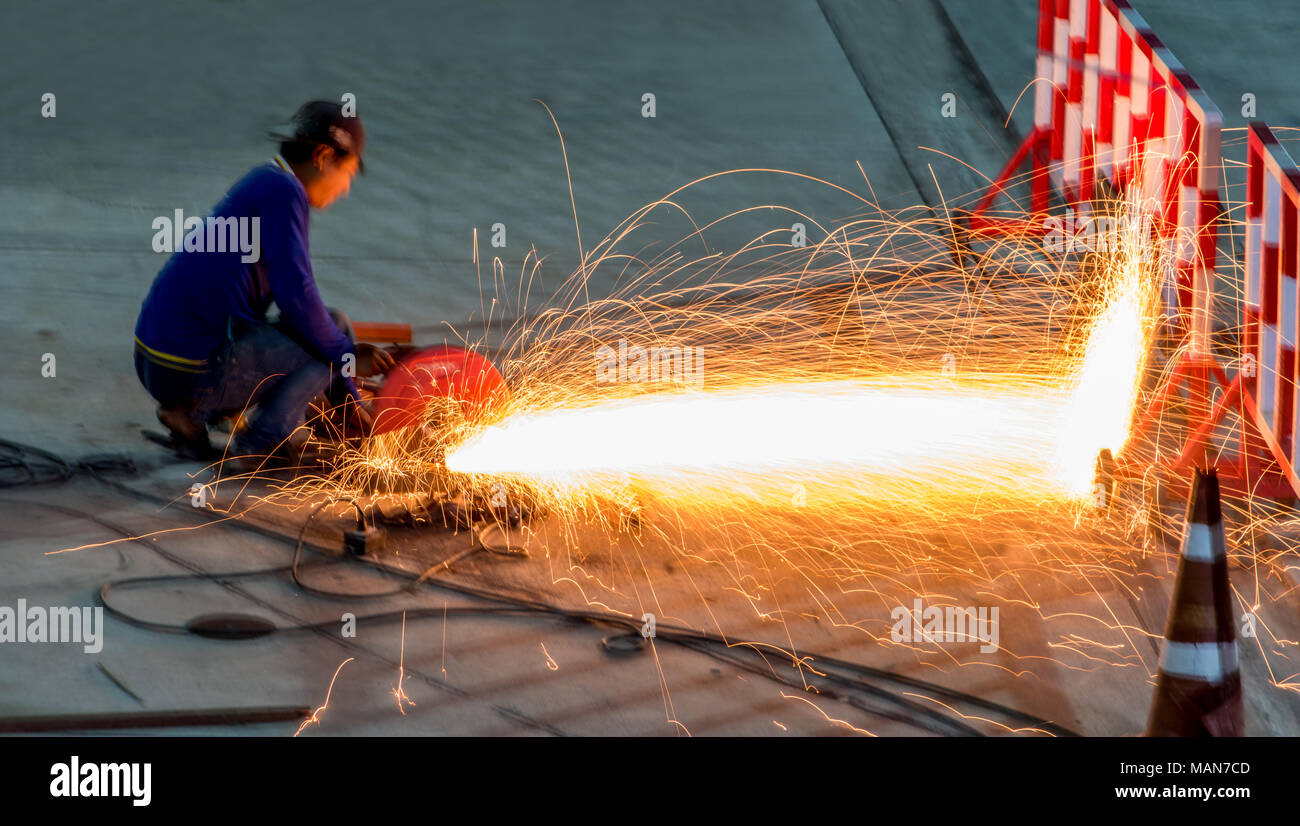 Un homme coupe acier avec un éclat rouge battant de métal découpé. Worker cutting metal avec une meuleuse. Banque D'Images