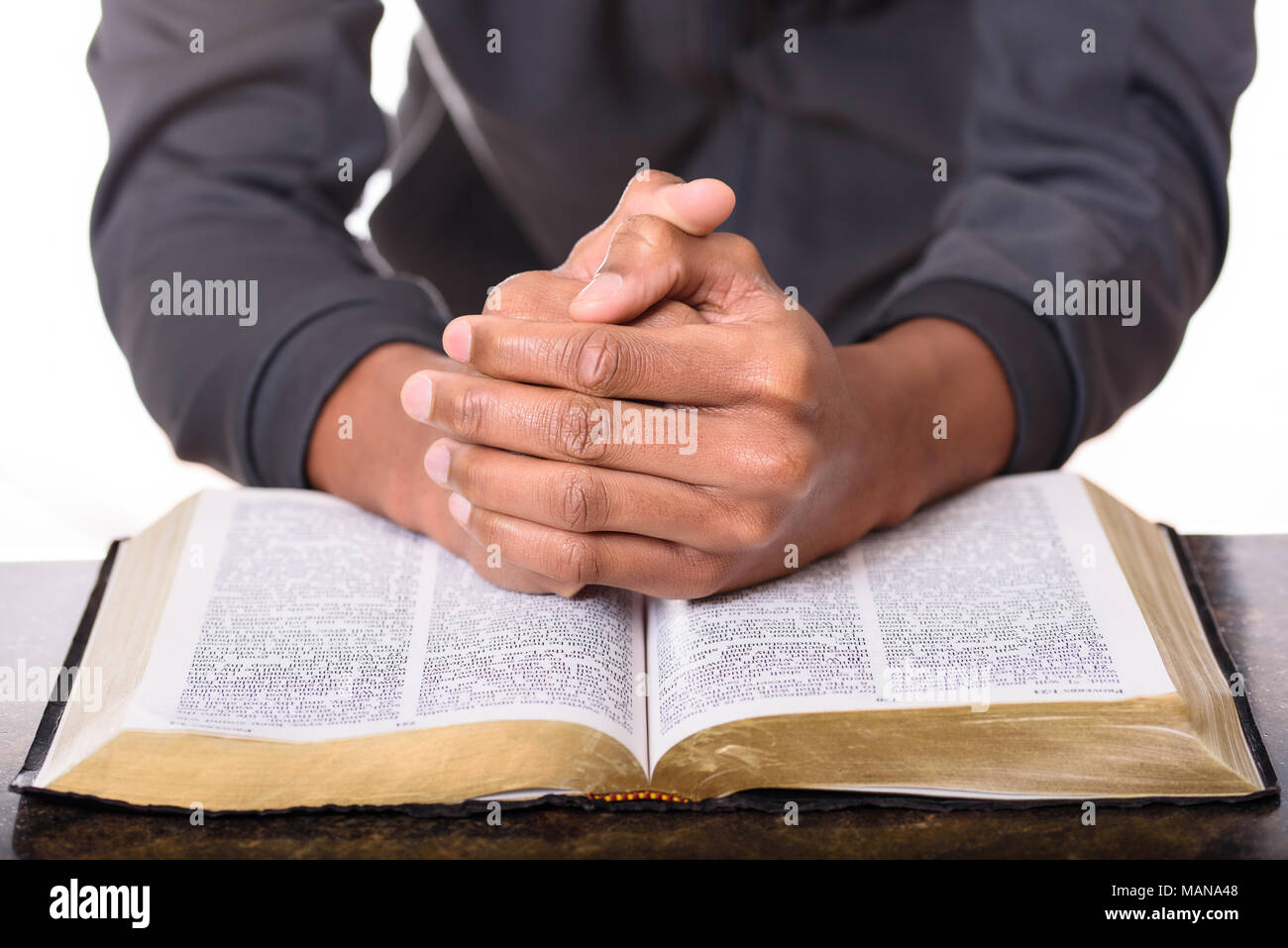 Mains d'un jeune homme plié priant sur une Bible, mains sur soft focus Bible Banque D'Images