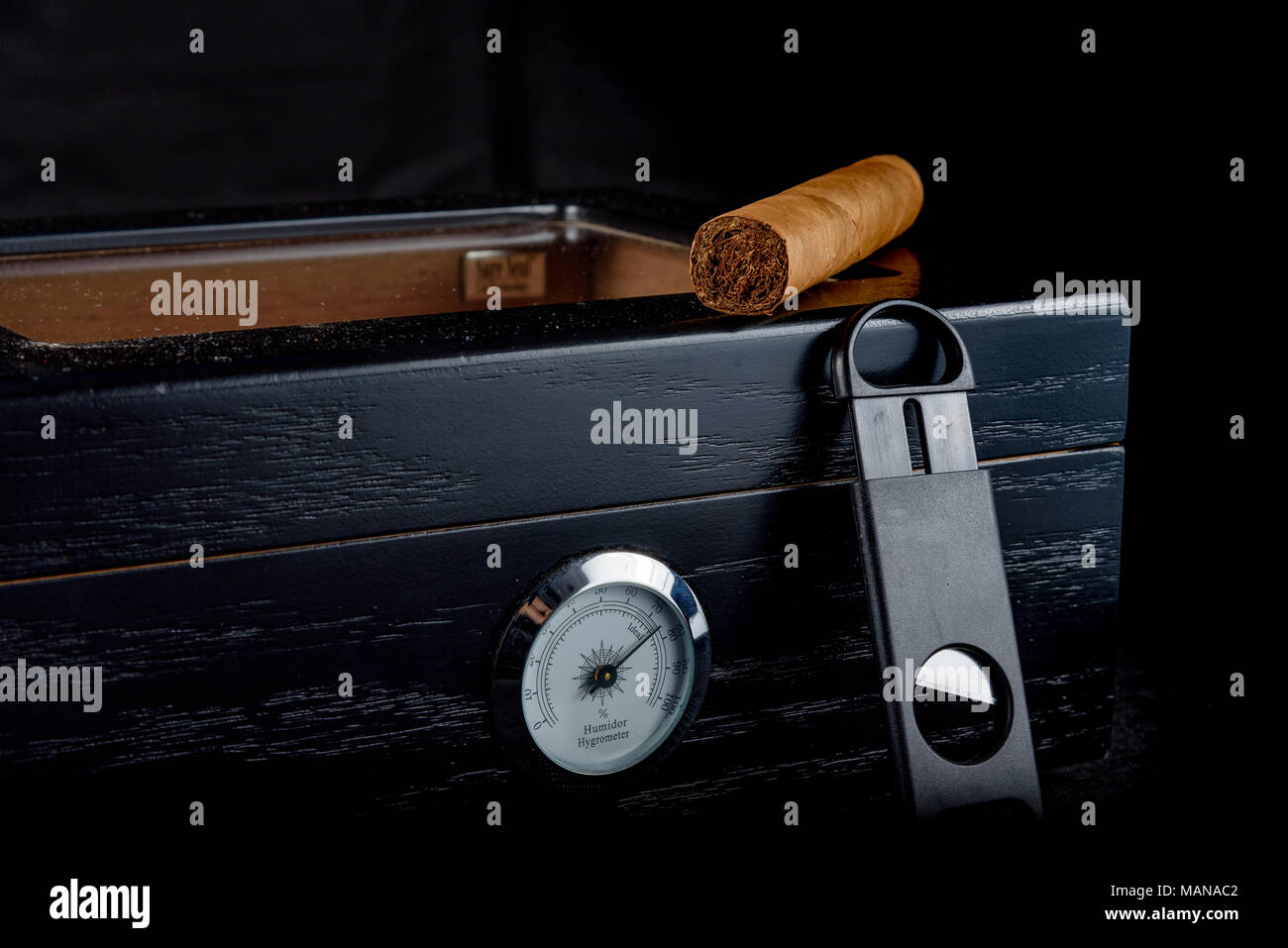 Une riche odeur de cigare, sur un humidor noire à côté d'un coupe-cigare tout droit. Fond noir Banque D'Images