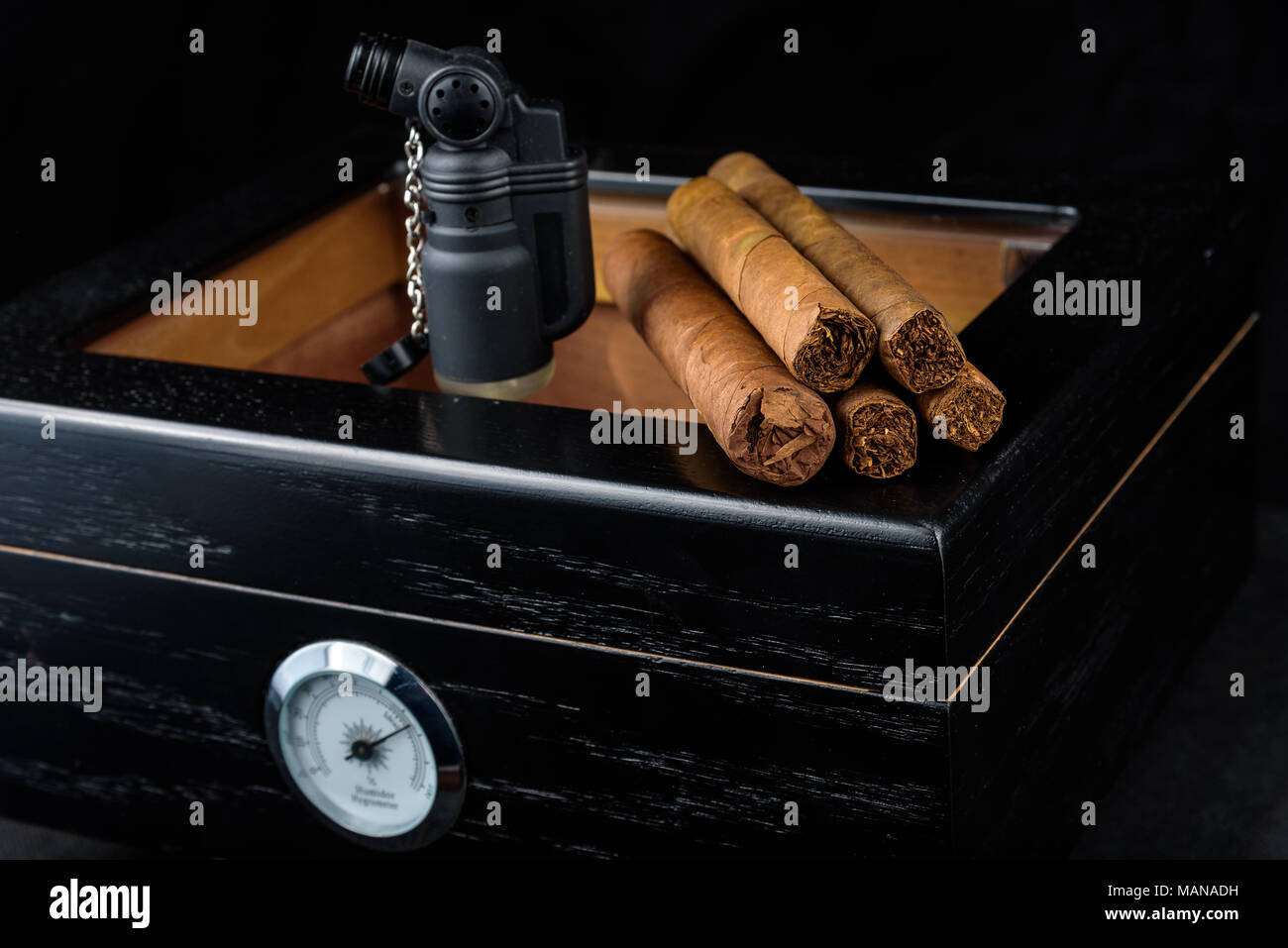 Une torche au butane noir et un tas de produits frais au-dessus d'une cave à cigares noire. Fond noir Banque D'Images