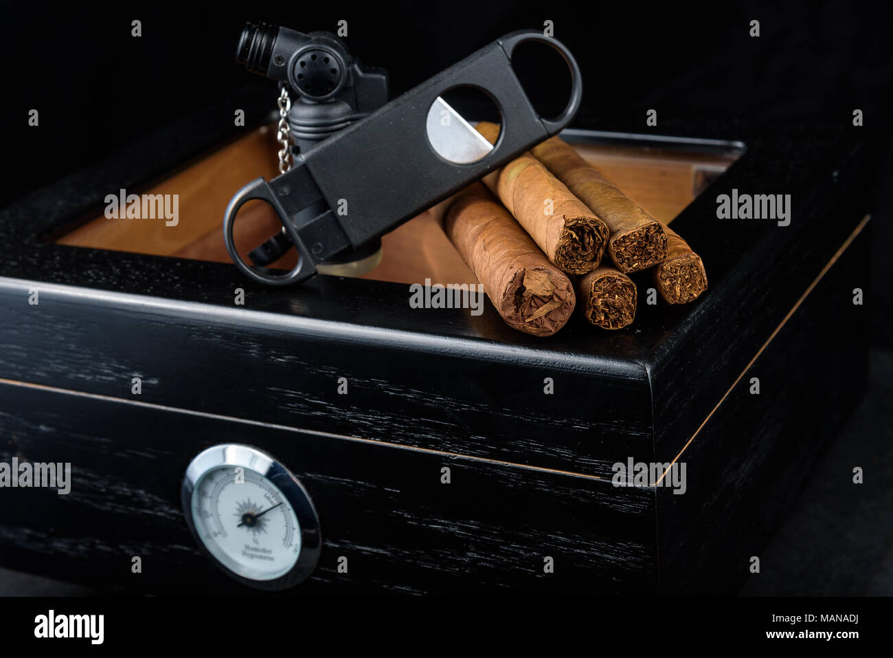 Une torche au butane noir, droit, coupe et un tas de produits frais au-dessus d'une cave à cigares noire. Fond noir Banque D'Images