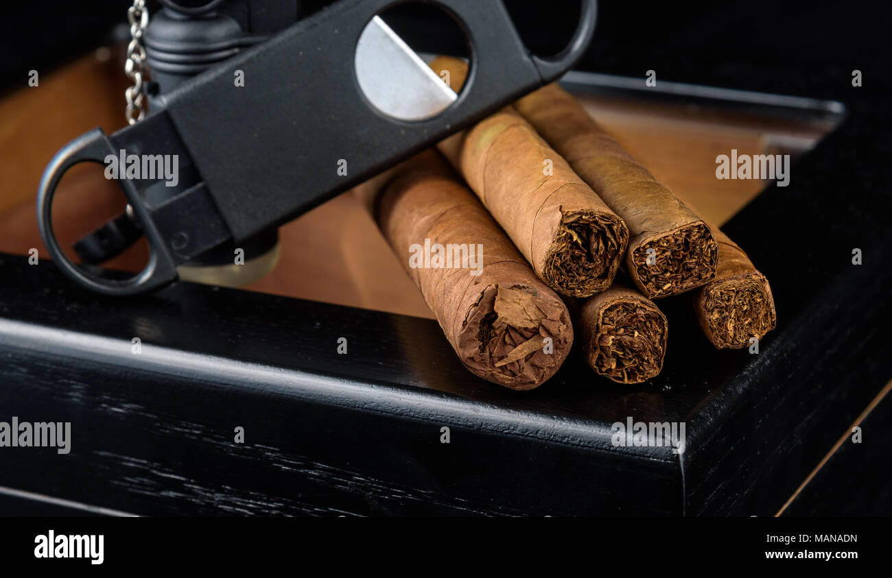 Une torche au butane noir, droit, coupe et un tas de produits frais au-dessus d'une cave à cigares noire. Fond noir Banque D'Images