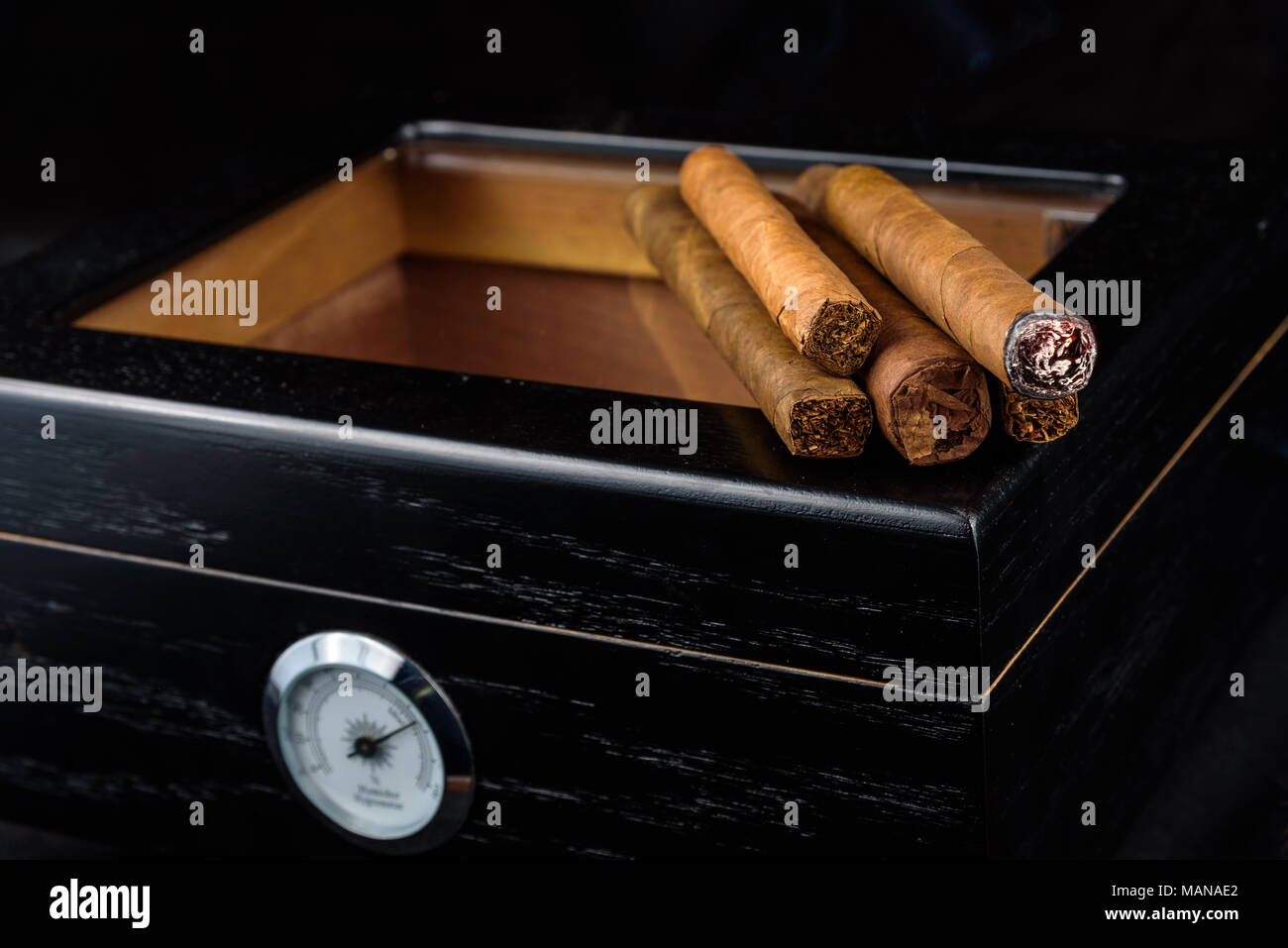 Un tas de produits frais avec des cigares d'un cigare allumé et fumeurs noirs au-dessus d'une cave. Fond noir Banque D'Images