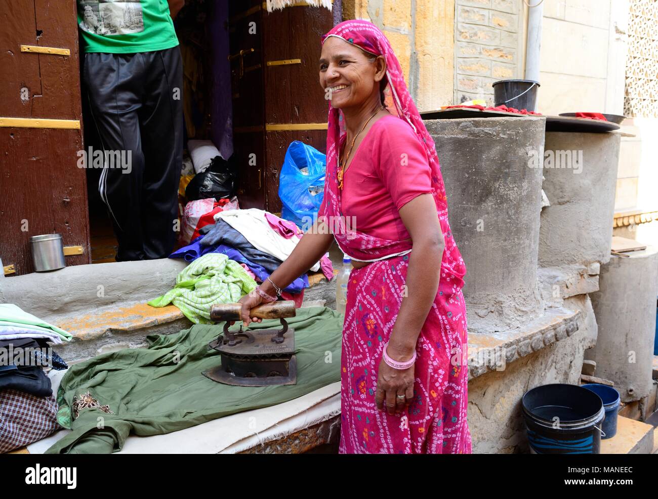Smiling woman wearing a pink sari en utilisant un vieux fer à repasser rempli de charbon de bois pour repasser les vêtements jailsamer Rajashan Inde Banque D'Images