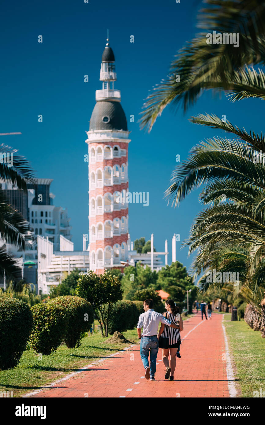 Batumi, Géorgie, l'Adjarie. L'homme et de la femme en train de marcher dans la piste cyclable en front de mer près de l'ancienne tour avec Restaurant en journée ensoleillée Banque D'Images