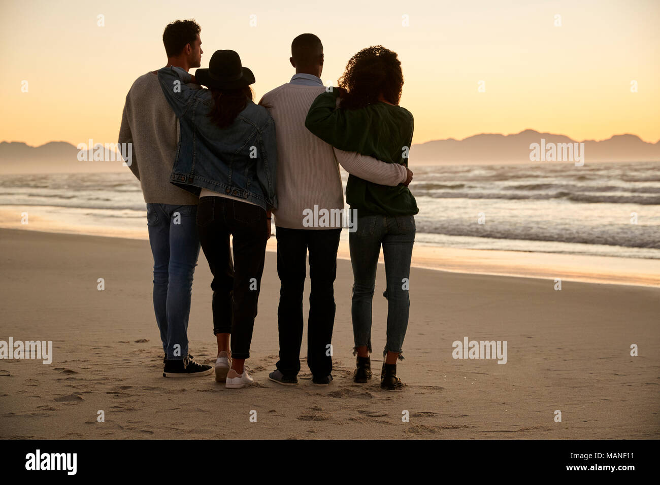 Groupe d'amis sur la plage en regardant le lever du soleil Ensemble d'hiver Banque D'Images