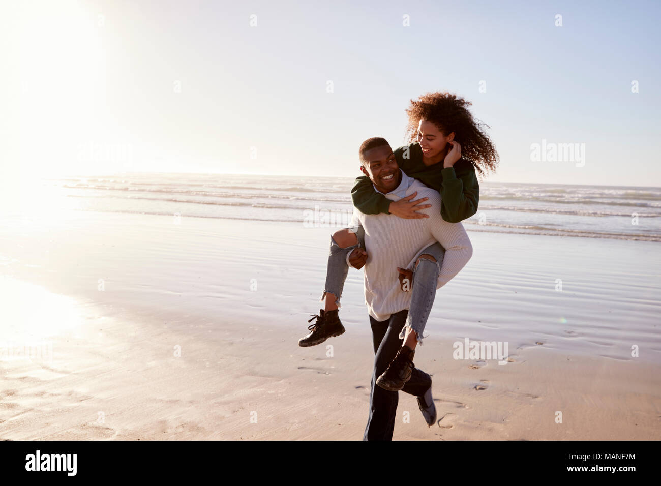 Man Giving Woman Piggyback sur Winter Beach Locations Banque D'Images