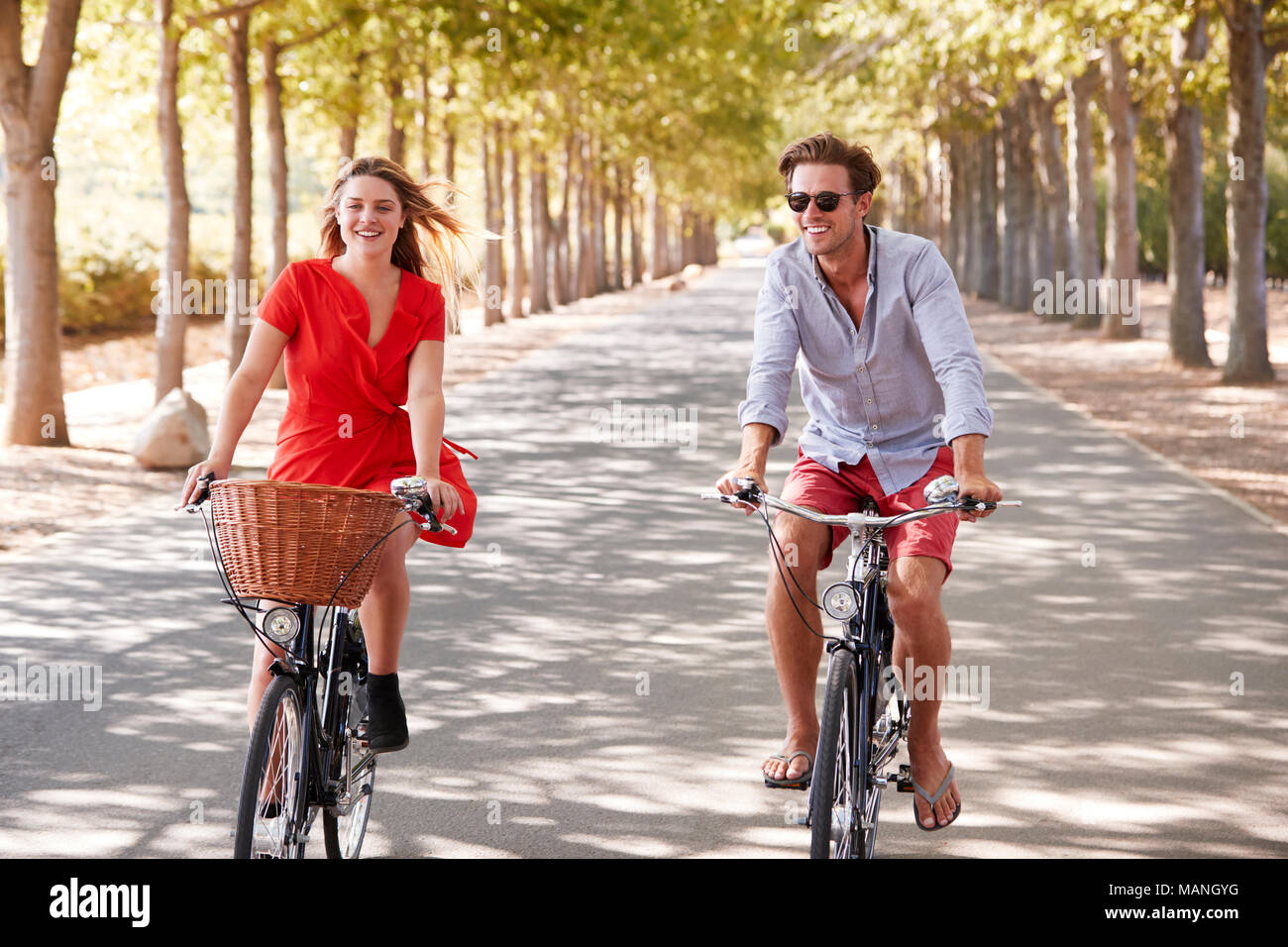 Les jeunes adultes blanc couple riding bikes sur une route bordée d'arbres Banque D'Images
