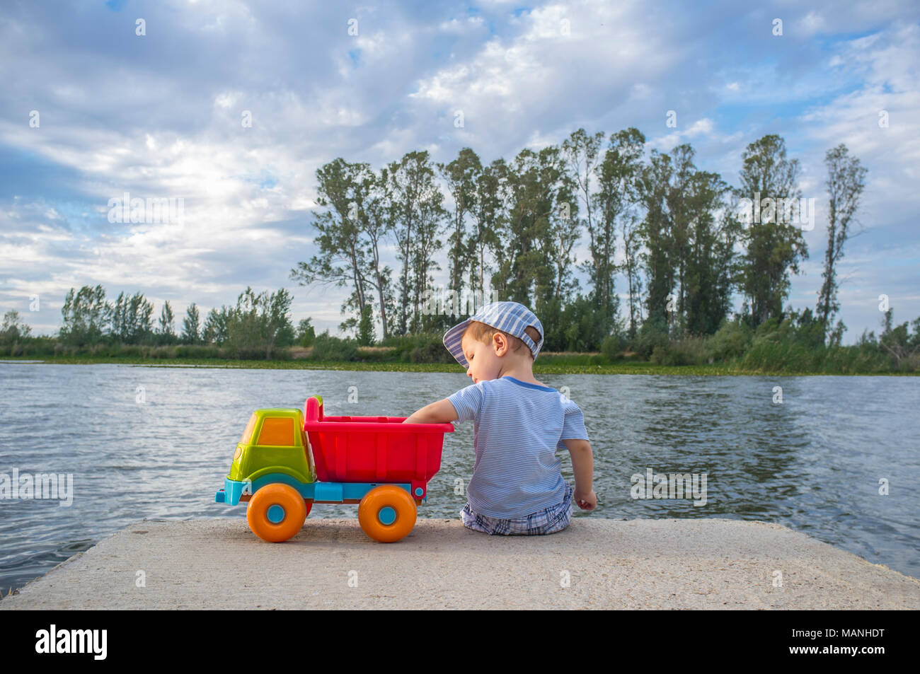 Deux ans Garçon jouant à Riverside avec dump truck. Il est assis sur la plate-forme fisher lancer des pierres Banque D'Images