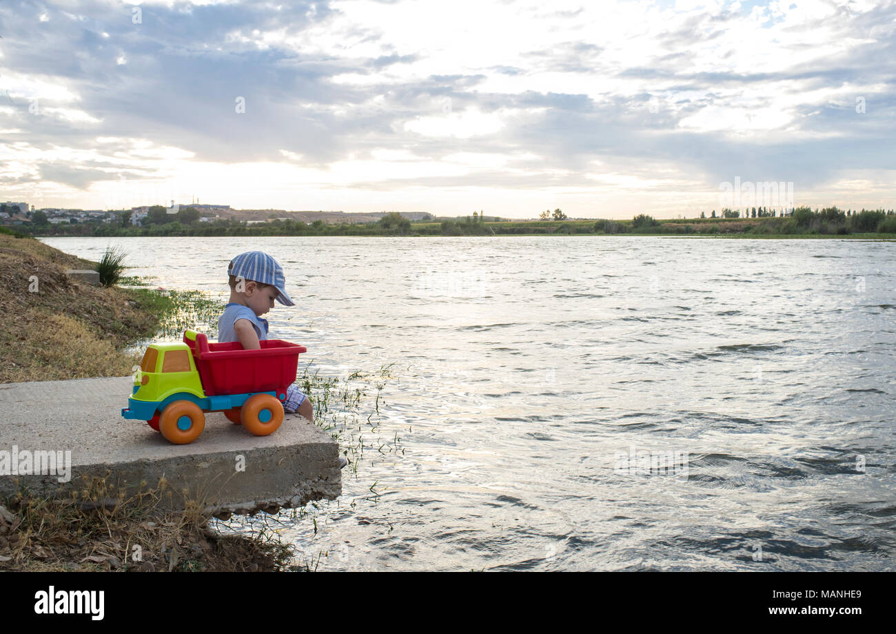 Deux ans Garçon jouant à Riverside avec dump truck. Il est assis sur la plate-forme fisher près de la ville de Badajoz Banque D'Images