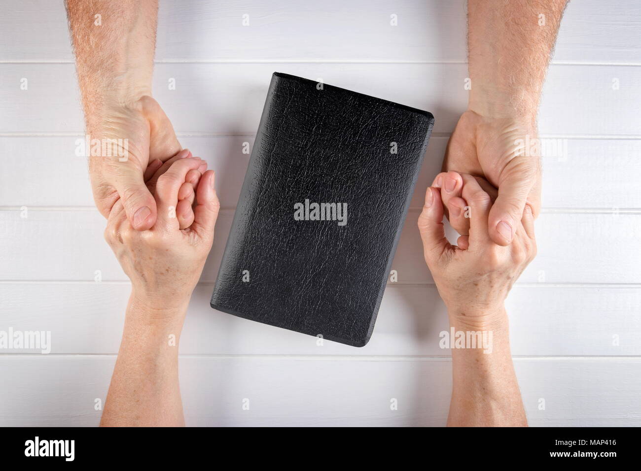 De l'homme et la femme/mari/femme tenant les mains autour d'une Sainte Bible sur blanc bois board Banque D'Images