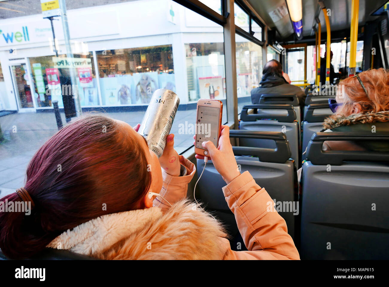 Les jeunes femmes s'assit sur le bus à l'arrêt de bus la lecture de messages texte et de boire une boisson énergétique peut de Banque D'Images