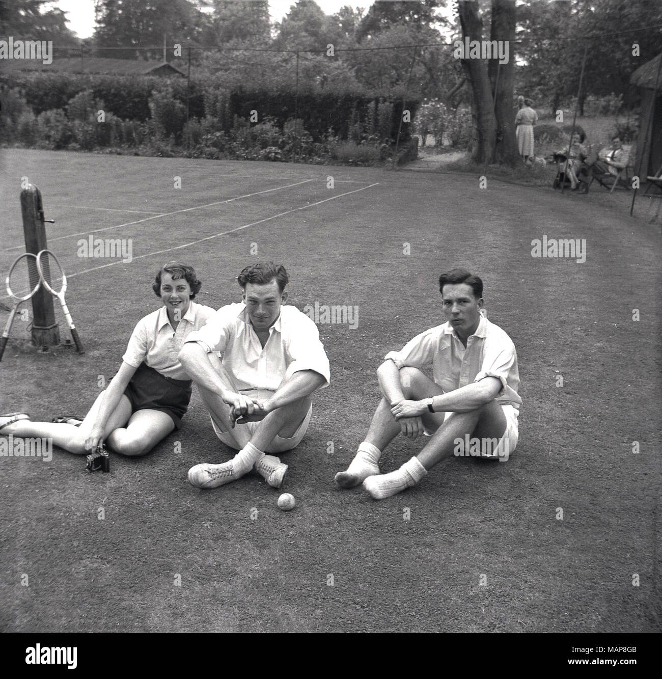 1954, historiques, les joueurs assis sur l'herbe, se détendre après une partie de tennis sur gazon à la maison de campagne du Bonham-Carter, Wyck Place, près de Alton, Hampshire, England, UK. Banque D'Images