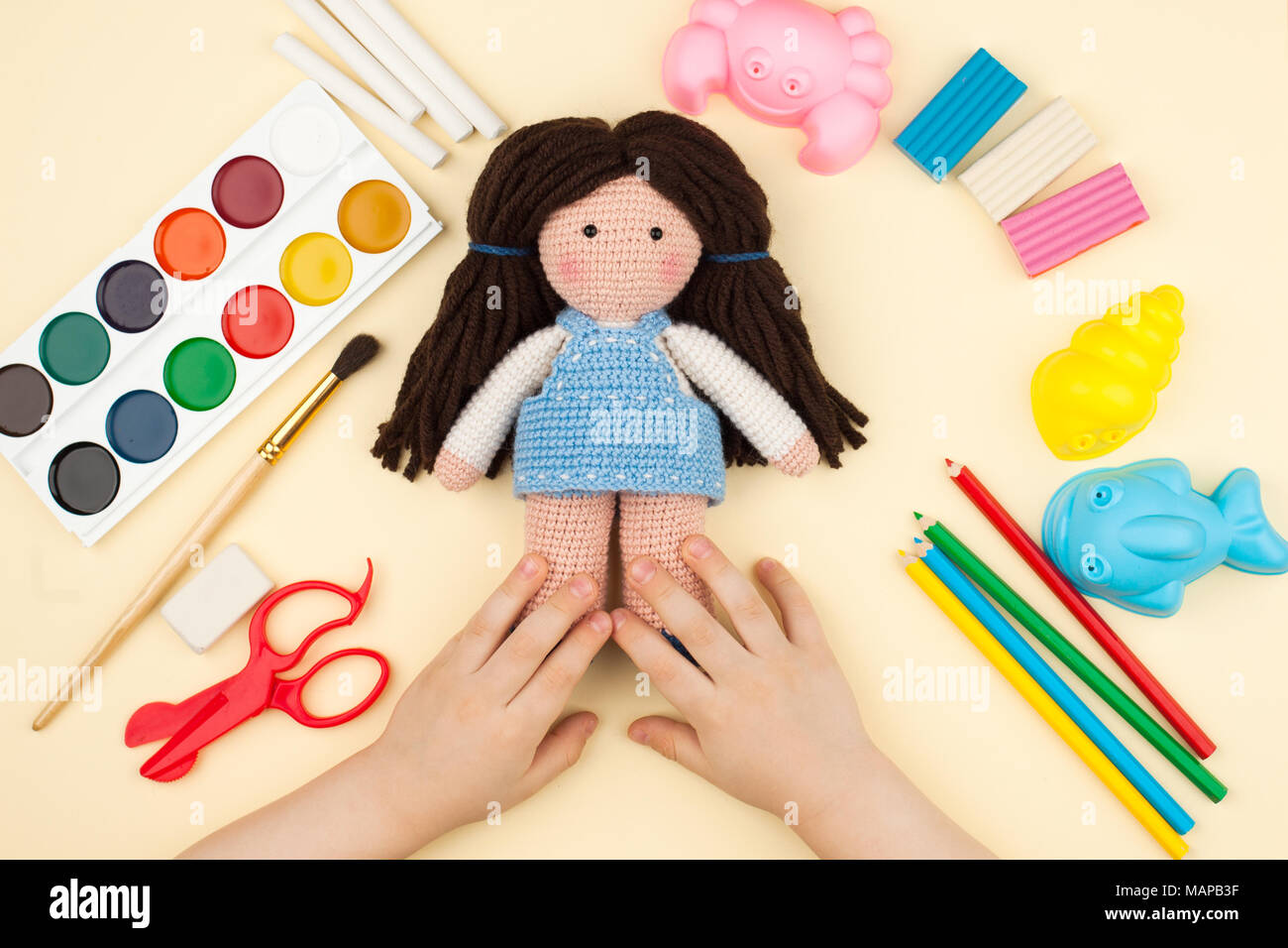 L'enfant est assis à la table avec des objets pour la créativité, dessin et loisirs, est titulaire d'une poupée en crochet dans les mains, une vue de dessus Banque D'Images