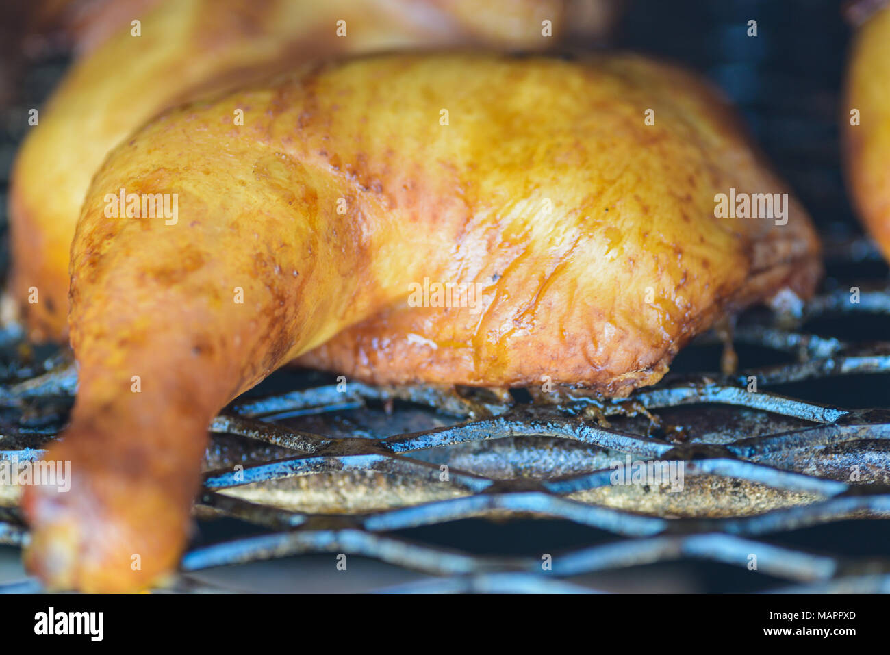 Poulet fumé sur grill, Close up de jambe et la cuisse avec peau dorée. Fond noir de smokehouse. Profondeur de champ, selective focus. Banque D'Images