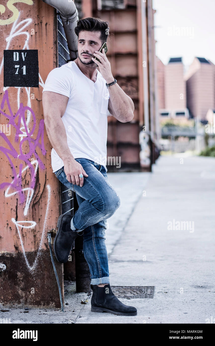 Beau jeune homme debout à l'extérieur dans l'environnement urbain sur les escaliers en métal, talking on cell phone Banque D'Images