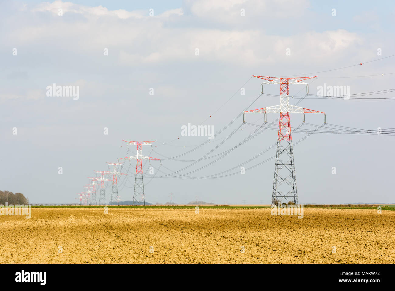 Une ligne électrique aérienne de tension soutenue par les tours de transmission rouge et blanche à travers la campagne française avec un champ labouré au premier plan. Banque D'Images