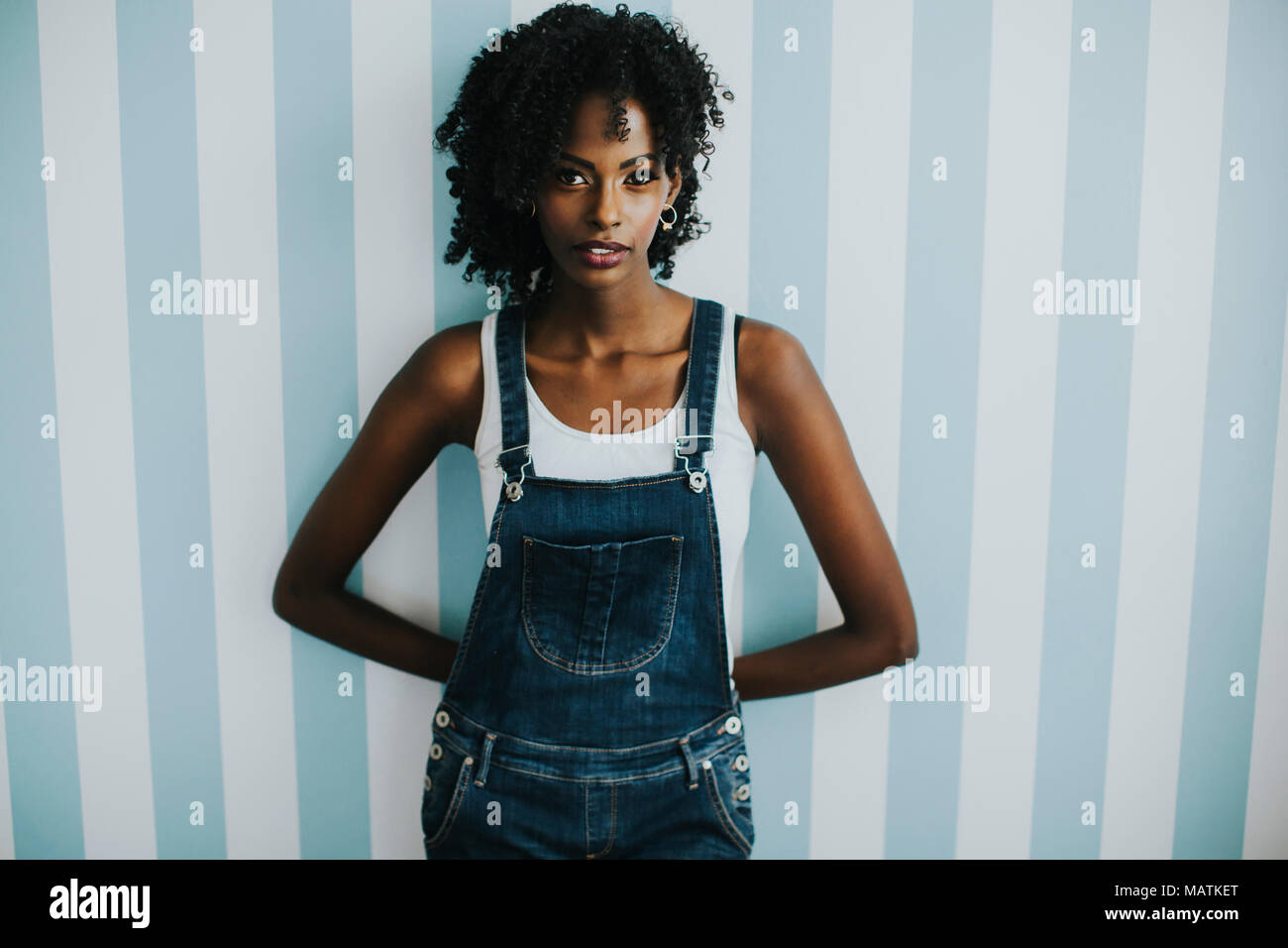 Pretty young african american woman posing in jeans pantalons par le mur dans la chambre Banque D'Images