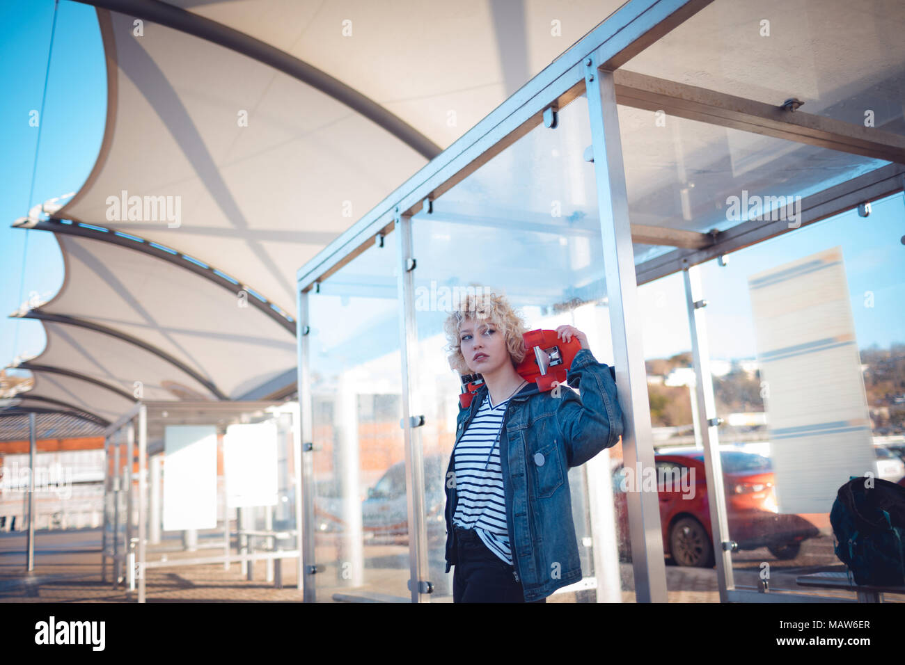 Woman holding skateboard at bus stop Banque D'Images
