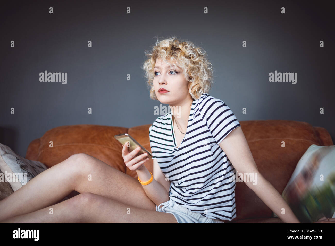 Woman using mobile phone in living room Banque D'Images
