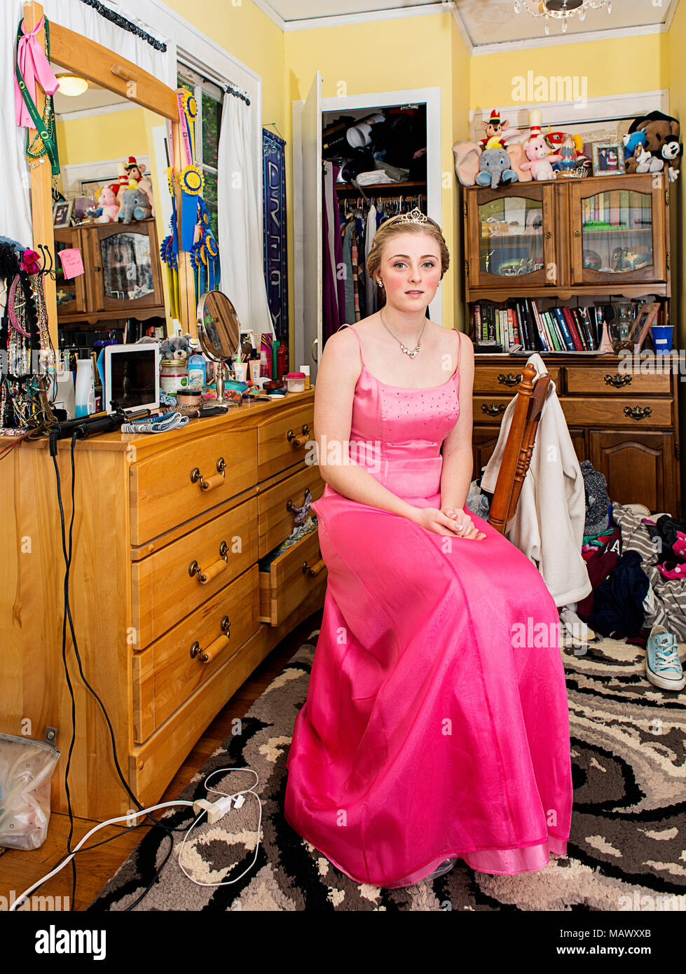 Une jeune femme assise dans sa chambre à coucher dans sa robe de bal. Banque D'Images