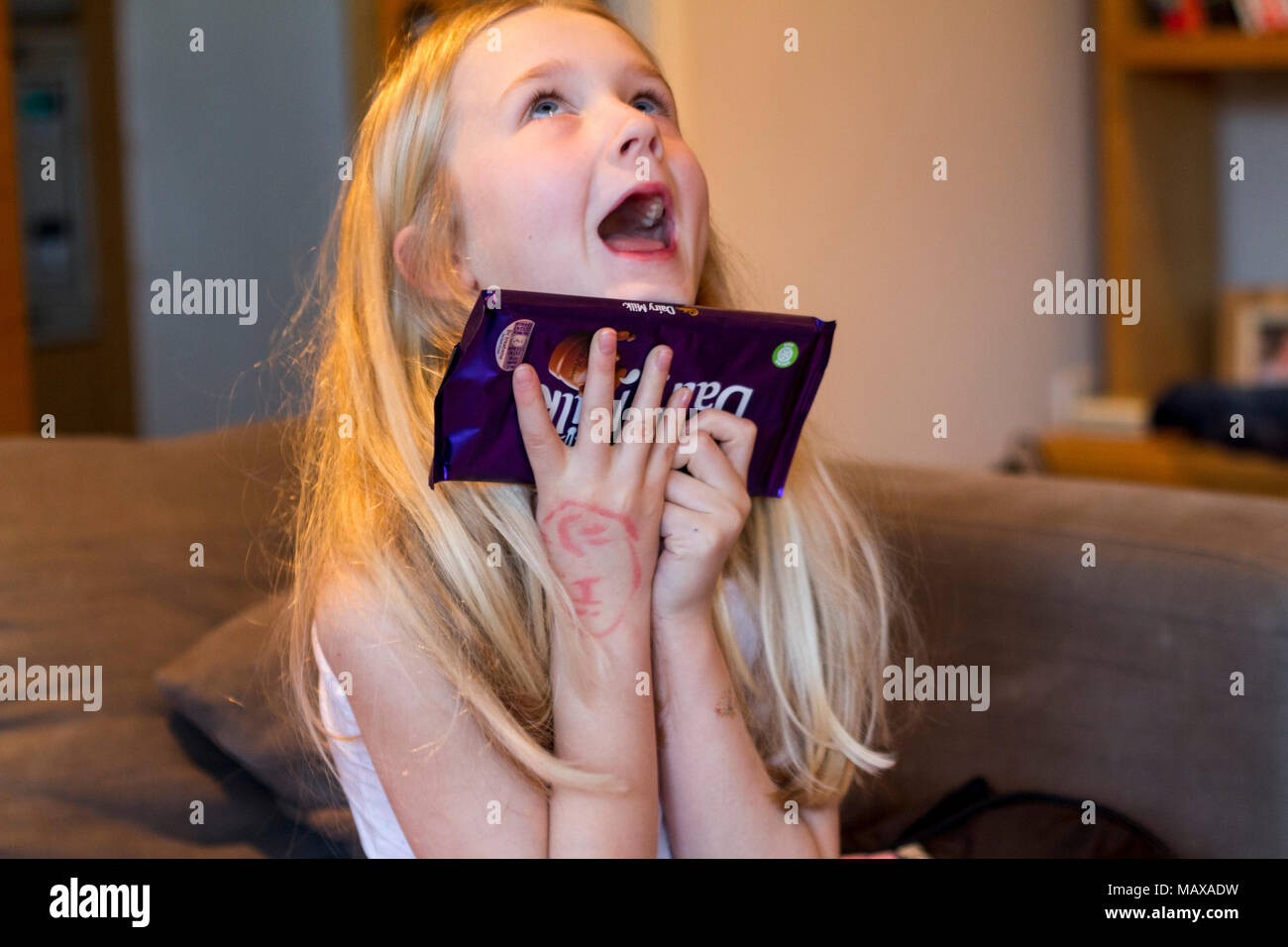 Heureux enfant kid girl blonde recevant une barre de chocolat Cadburys cadeau d'anniversaire, l'air très heureux, plein de joie, ravie en extase Banque D'Images