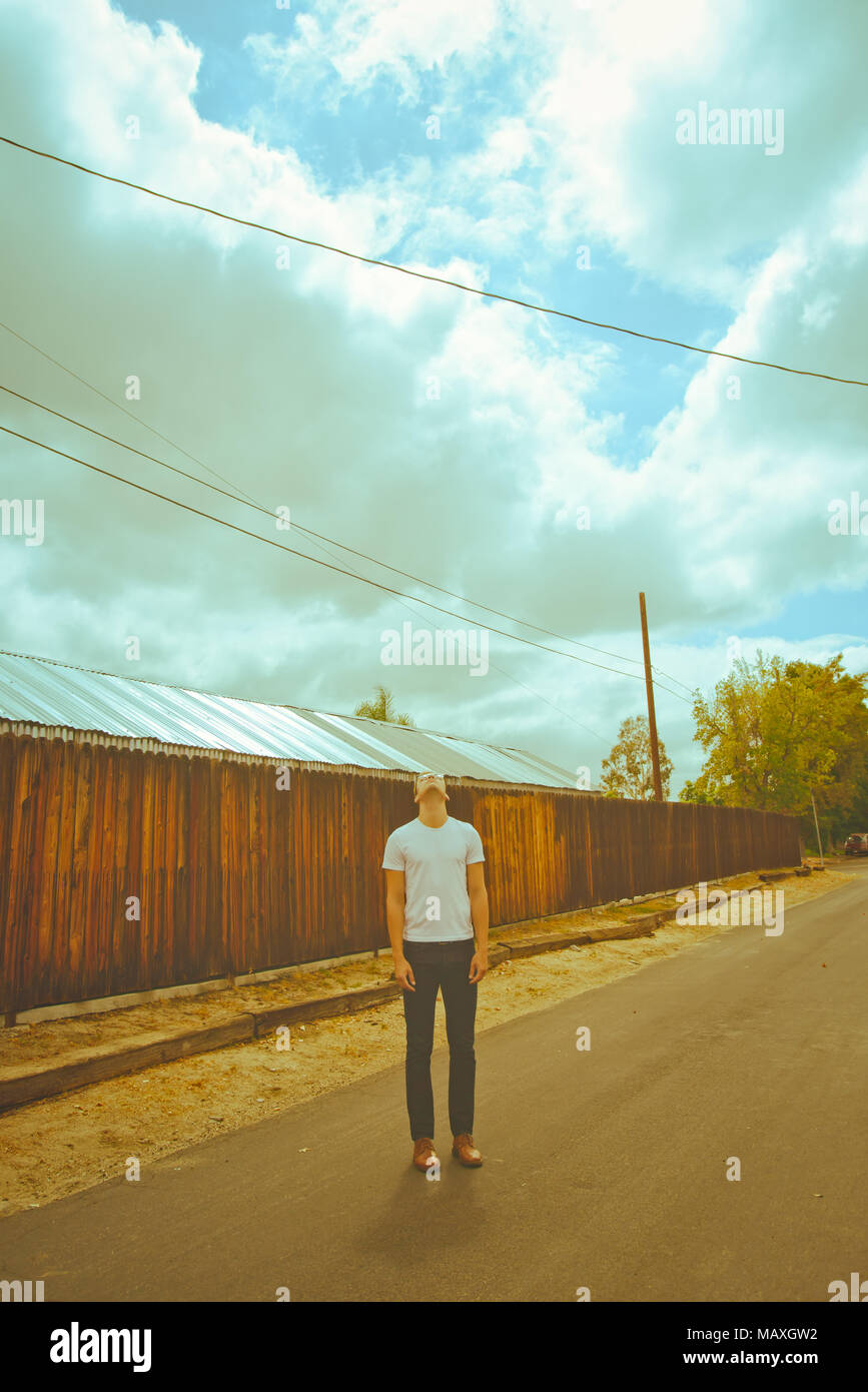 Un jeune homme de race blanche debout sur une petite route de campagne, à la recherche vers un ciel nuageux, désespoir ; un réveil spirituel concept. Banque D'Images