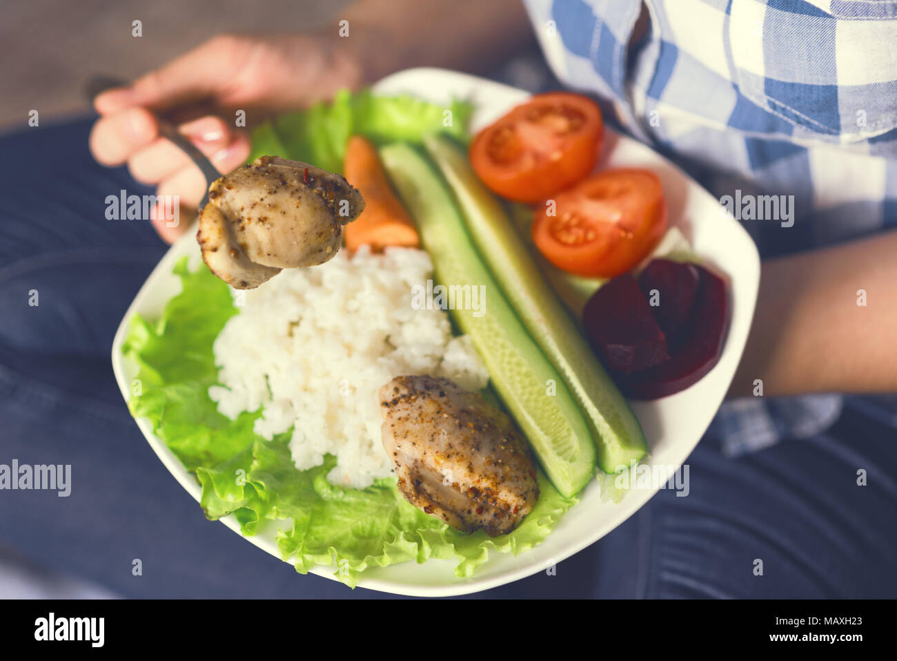 Une fille est titulaire d'une assiette de légumes et de poulet aux épices. Banque D'Images