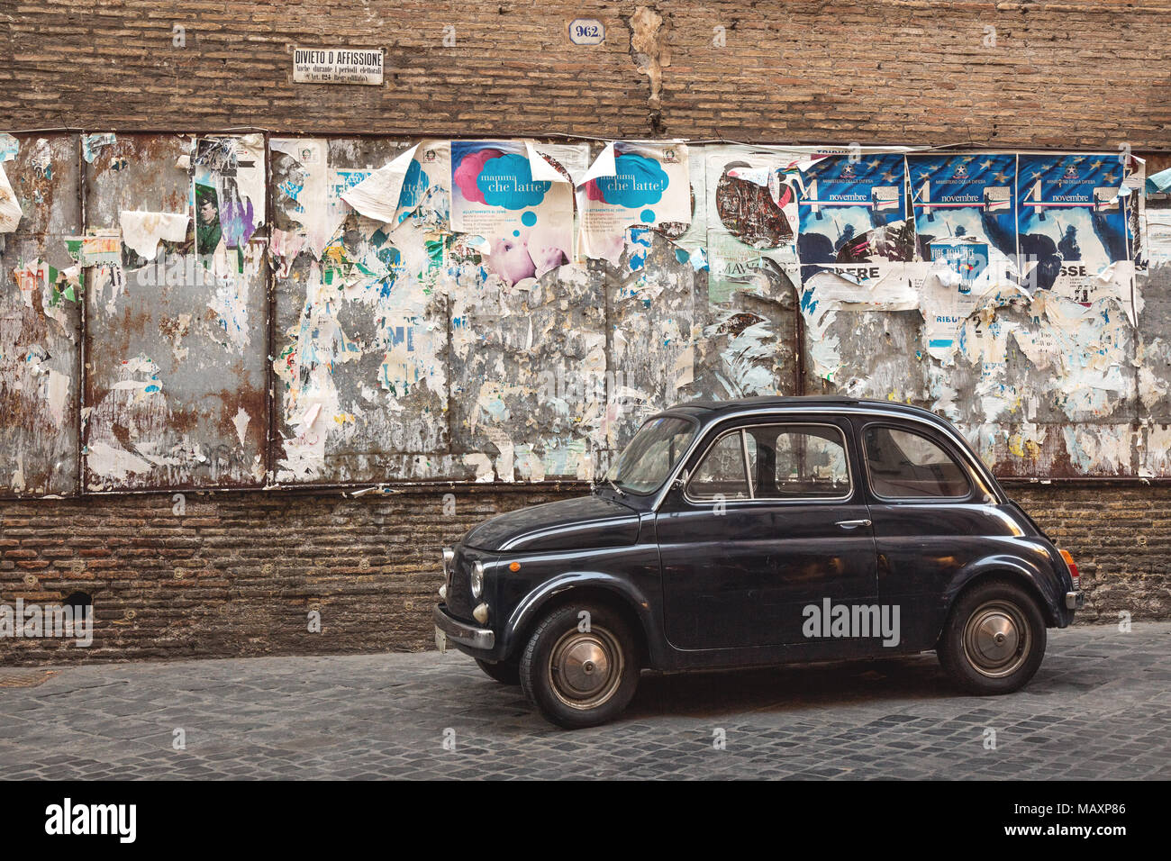 Une vieille Fiat 500 bleue garée dans une petite rue pavée, à Rome, Italie à côté de quelques vieilles affiches publicitaires. Banque D'Images