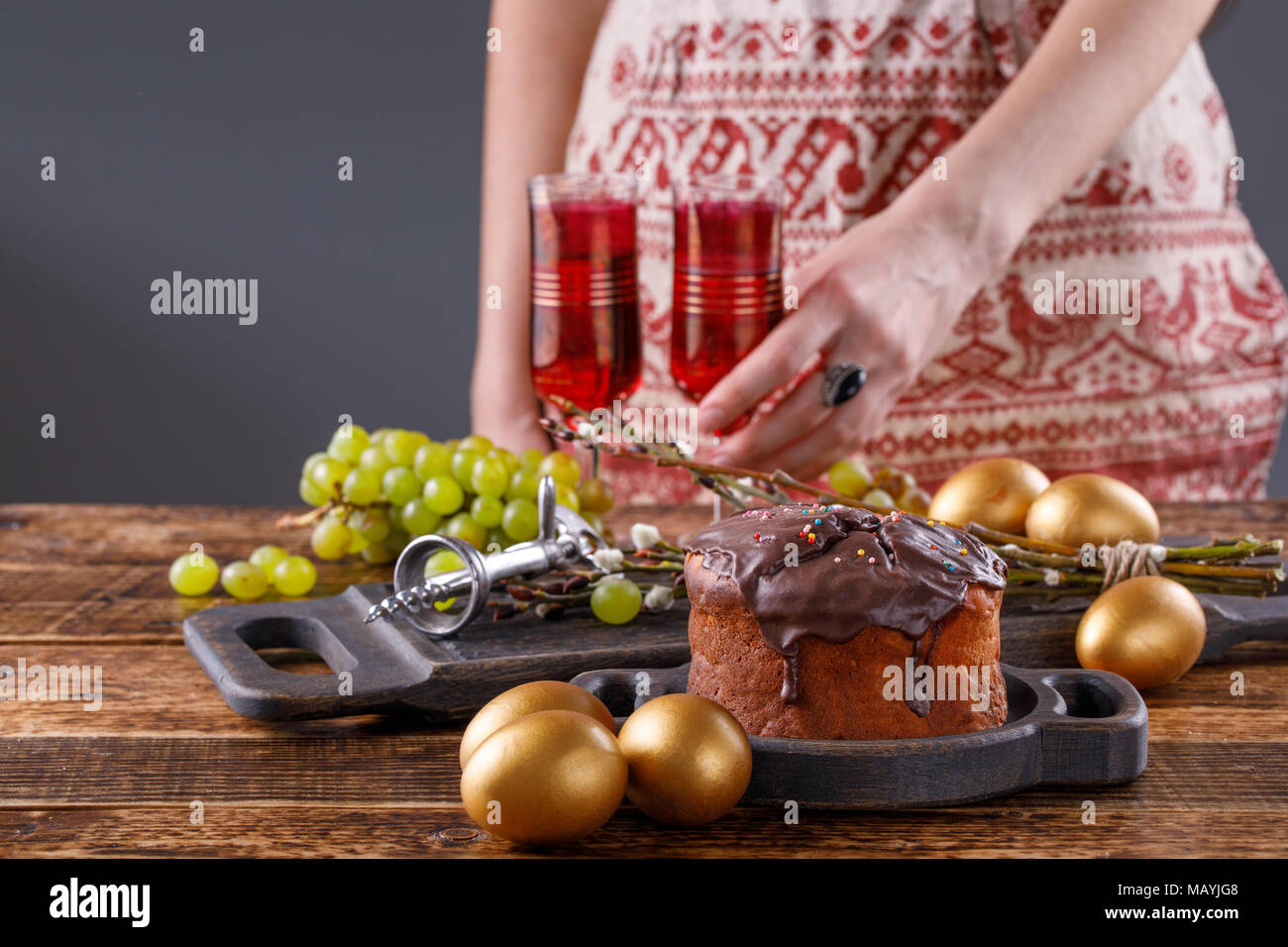 Accueil frais, gâteau de Pâques des oeufs d'or, le vin rouge en lunettes vintage, des raisins et des meubles anciens tire-bouchon sur la table. La fille est la pose pour table de fête Banque D'Images