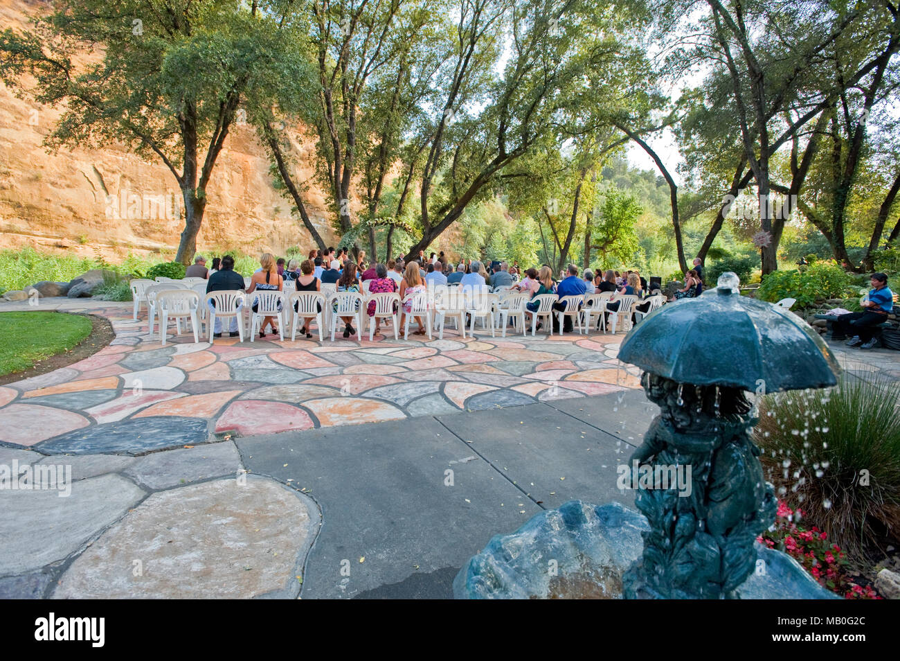 Un mariage en plein air à l'ombre des chênes en face d'une rivière à un lieu de la Californie, avec une statue de brun à l'avant-plan Banque D'Images