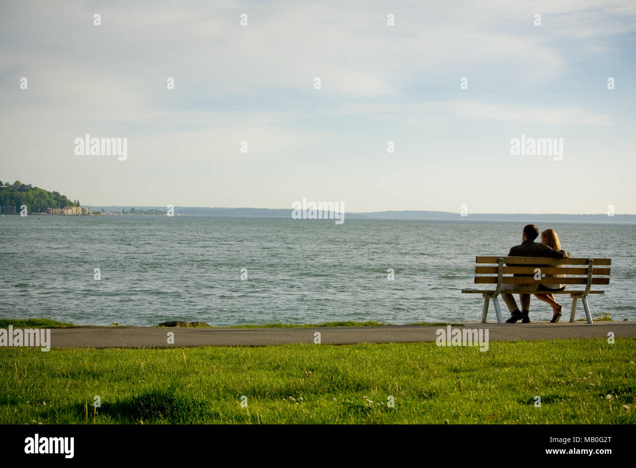 Un jeune couple assis à une chaise à l'extérieur, vers la mer à un parc au bord de l'eau dans le centre-ville de Seattle Banque D'Images