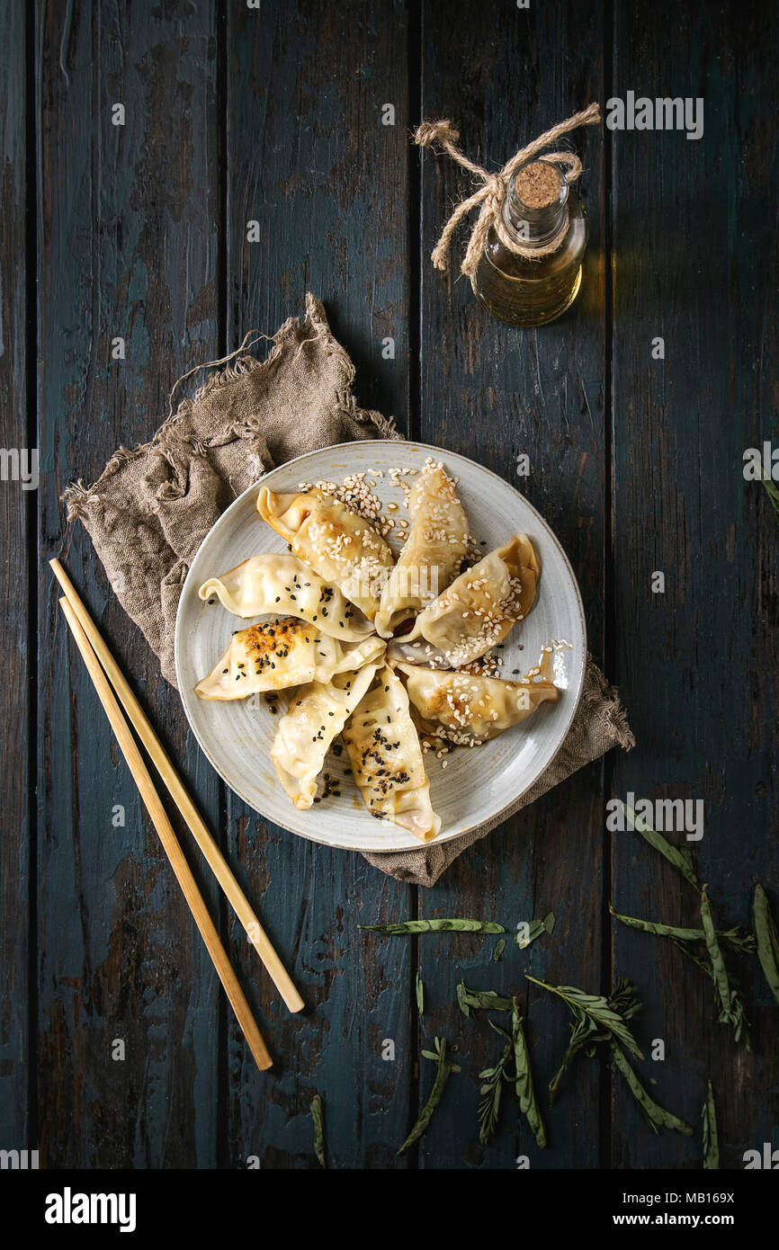 Les Gyozas raviolis frits potstickers asiatiques sur une plaque en céramique, servi avec des baguettes et bouteille de sauce sur planche en bois sombre arrière-plan. Vue de dessus, spa Banque D'Images