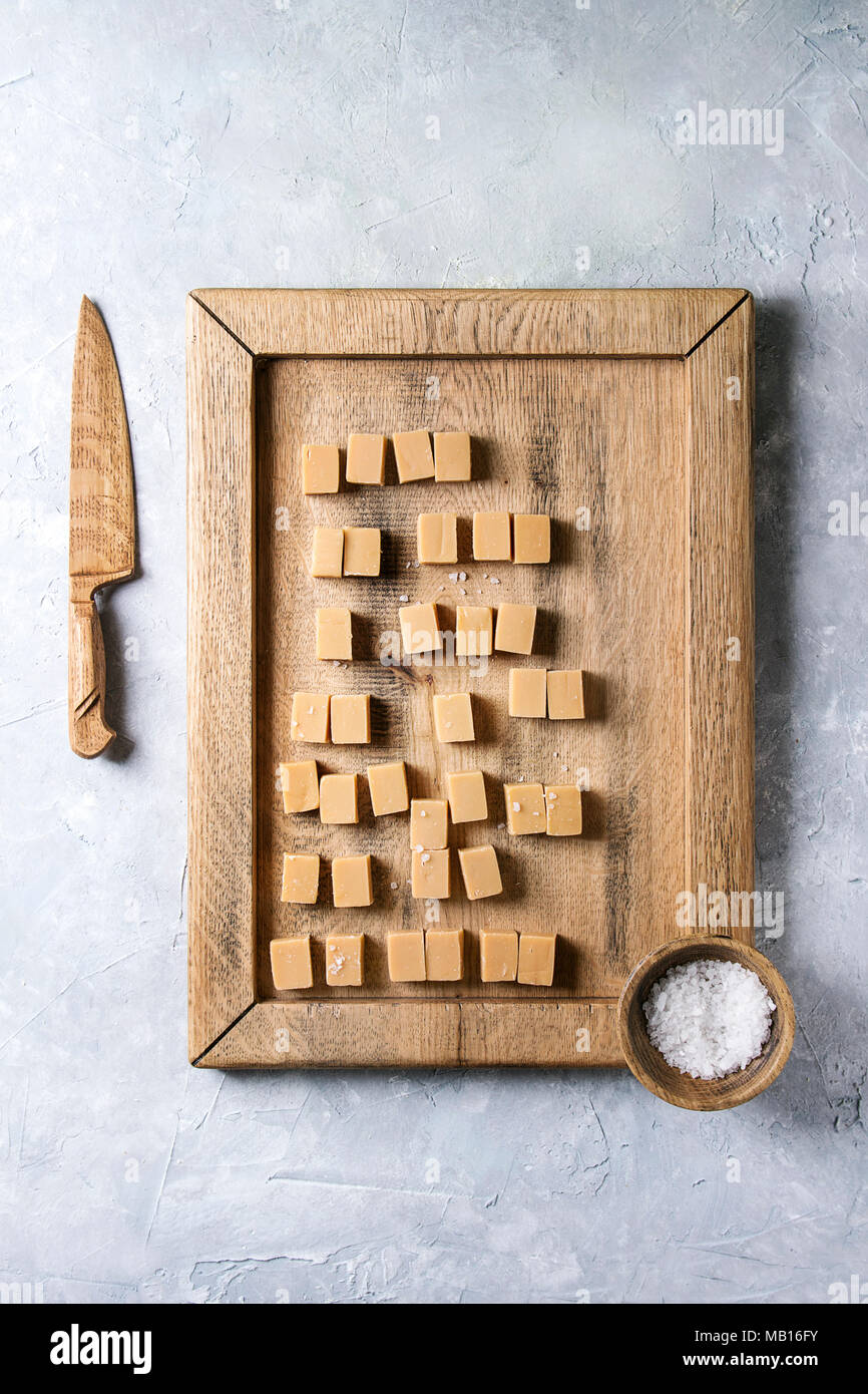 Fudge au caramel salé bonbons servis sur plateau en bois avec fleur de sel dans un bol en bois et couteau sur fond texture gris. Vue de dessus, de l'espace. Banque D'Images