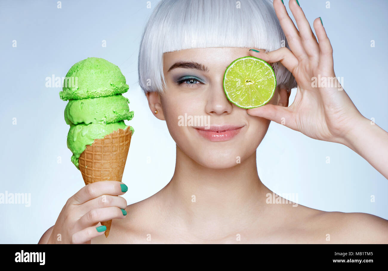 Funny young girl holding cornet gaufré avec de la glace et vert lime. Photo de smiling blonde girl sur fond bleu. Vie heureuse Banque D'Images