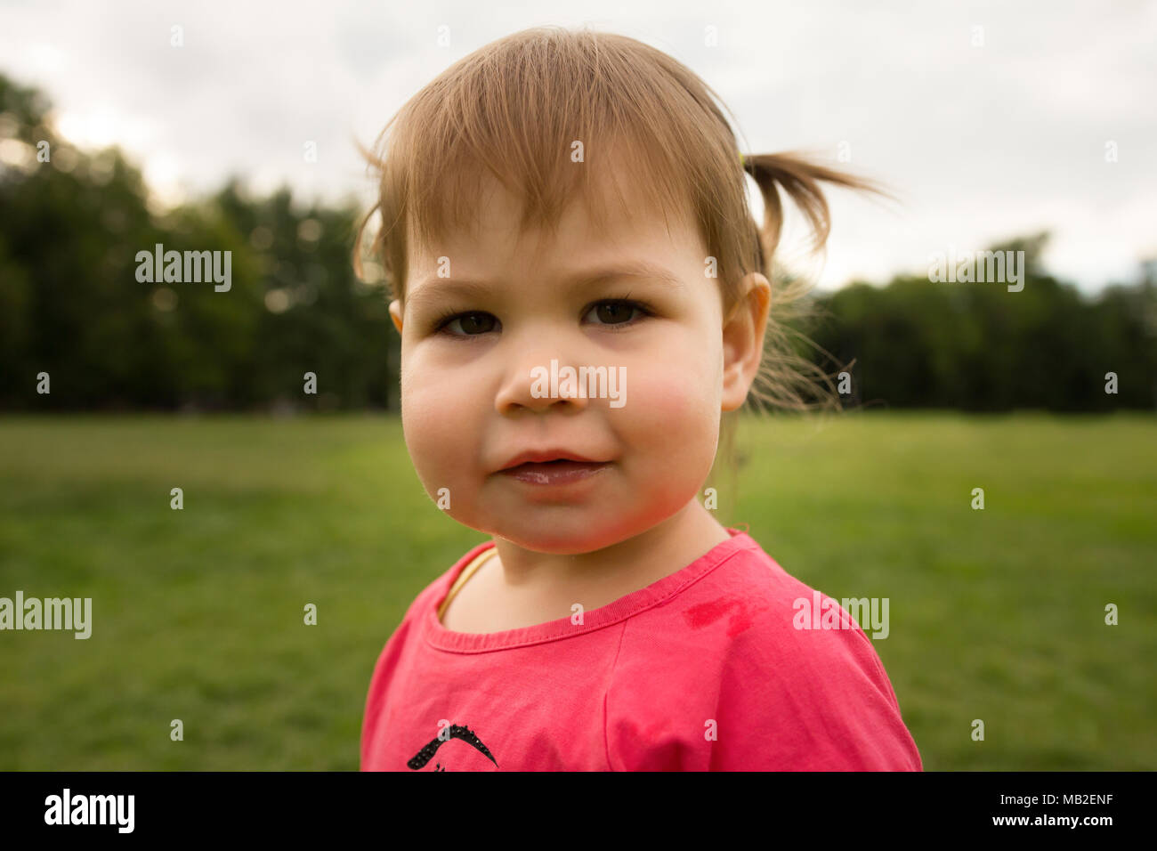 Cute Little girl en robe rose jouant dans le parc en face de l'herbe verte Banque D'Images